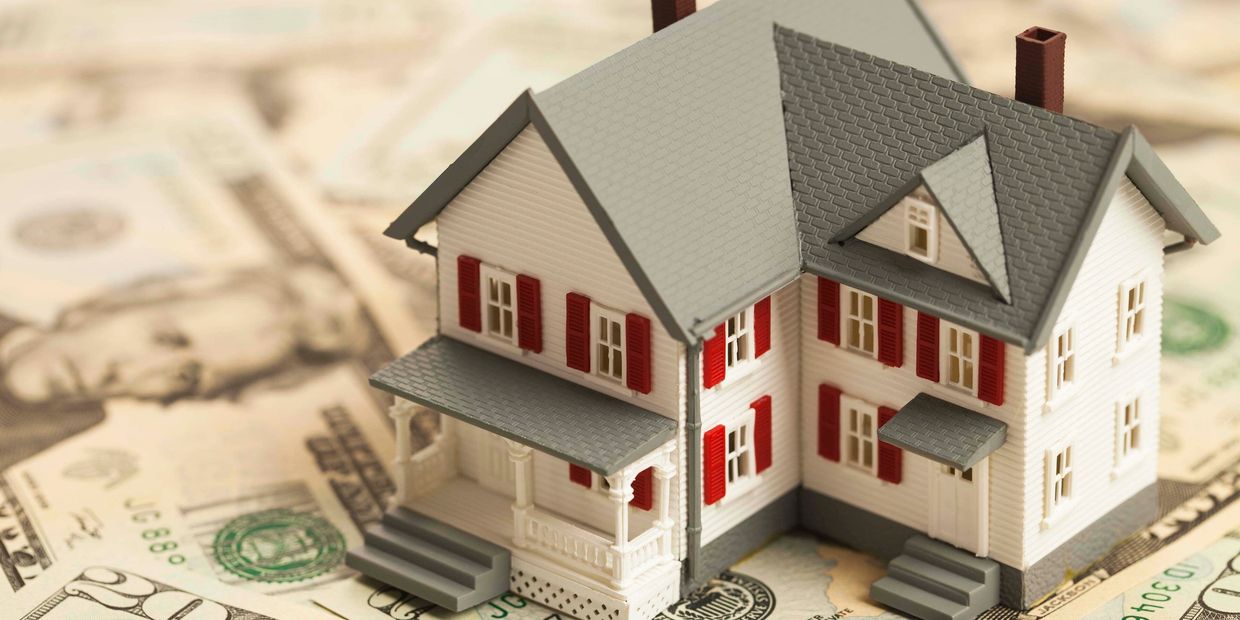 A miniature house model placed on U.S. dollar bills.