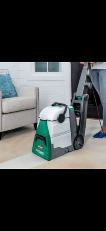 A person using a carpet cleaner on a beige carpet in a living room.