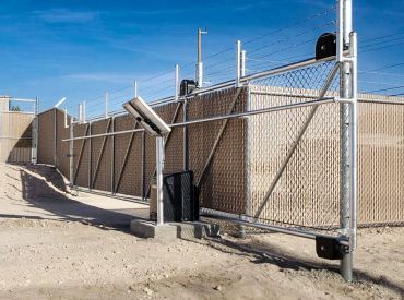 A secured metal gate with barbed wire under a clear blue sky.