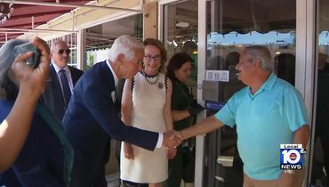A man in a suit shakes hands with a man in a blue shirt outside a building.