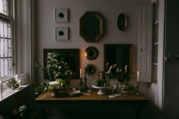 Dimly lit room with a styled buffet: fruit, flowers, candles, and decorative mirrors on the wall.