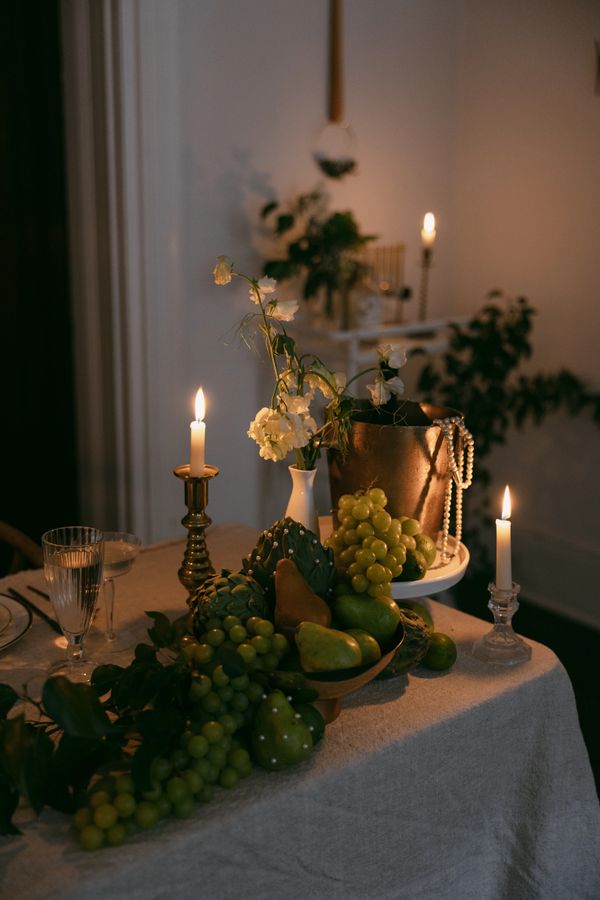 Warmly lit table with fruit, flowers, and candles.