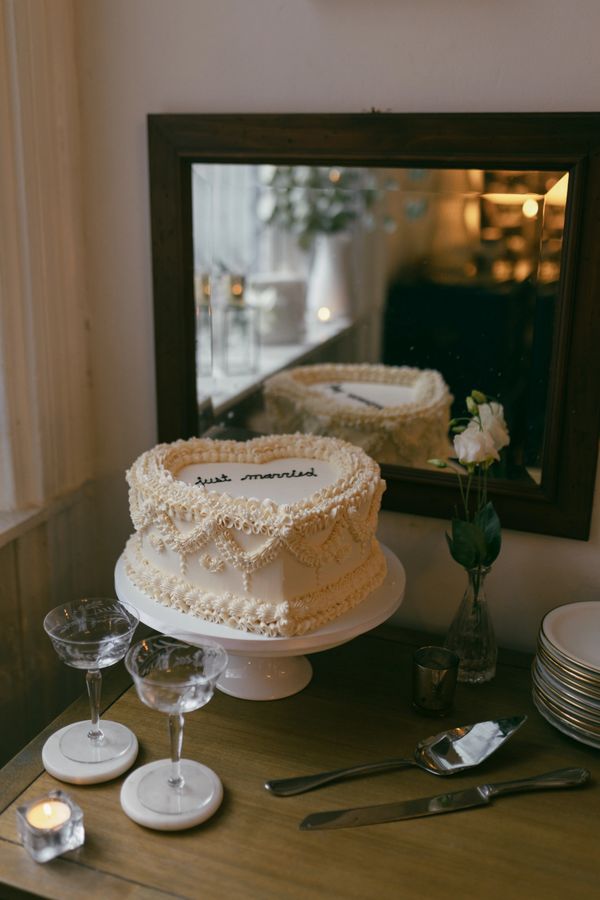 Elegant "Just Married" cake with lace detail, glasses, and serving utensils on a table with a mirror