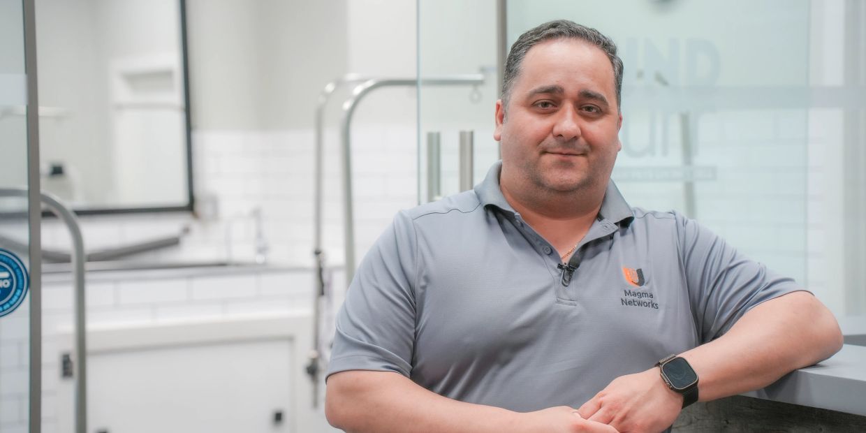 Man wearing a Magma Networks shirt leaning on a counter in a modern office.
