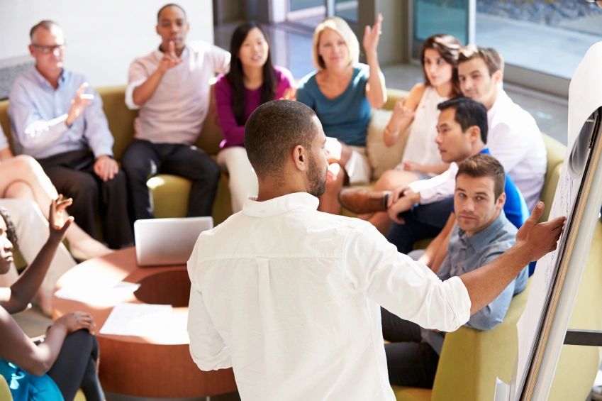 A group of adults in a circle doing planning led by a facilitator making notes on a flip chart