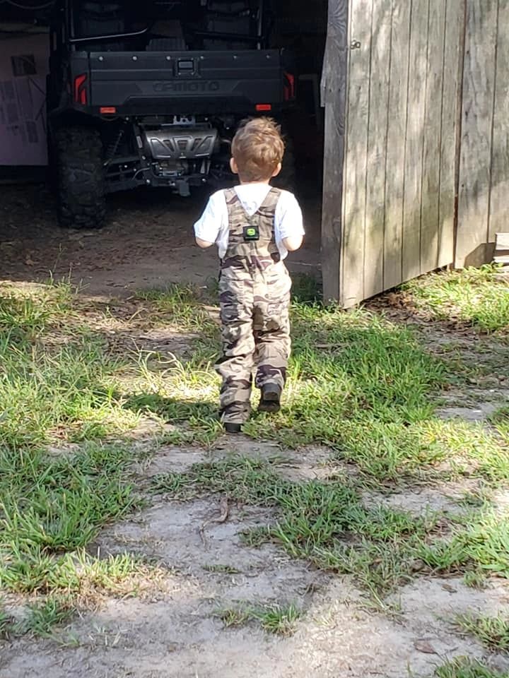 Young boy, our grandson, in overalls walking to shed where side by side utv is parked