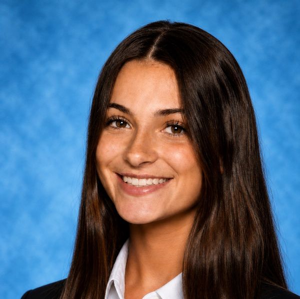 Young woman with long brown hair smiling against a blue background.