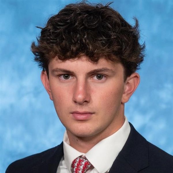 Young man in formal suit with curly hair against blue background.