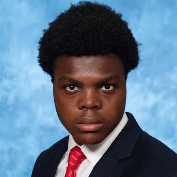 Young man in formal suit and red tie against blue backdrop.