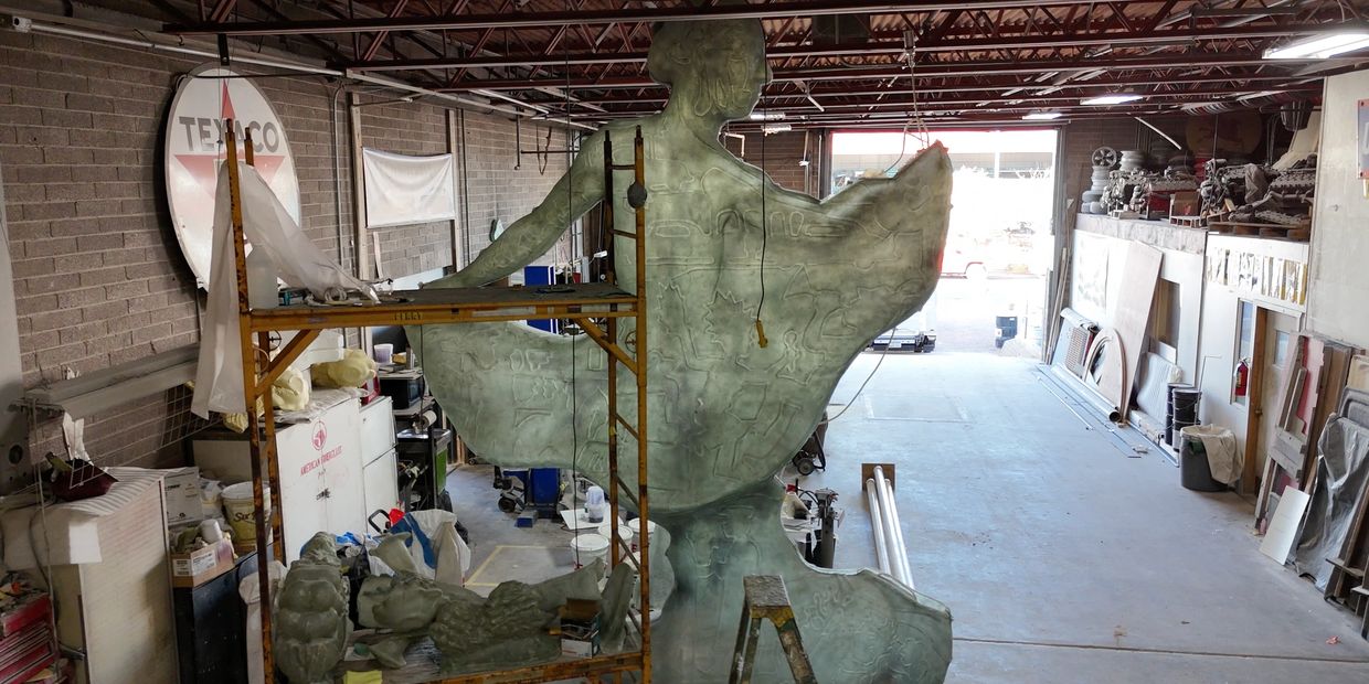 Large sculpture in workshop with scaffolding and tools around.
