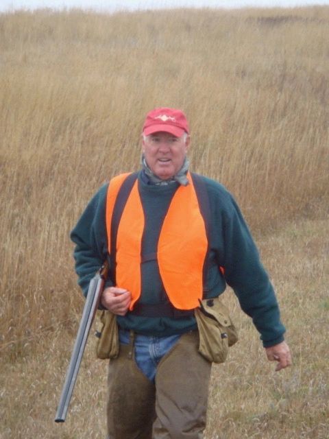 Man in orange vest and red cap holding a shotgun outdoors.