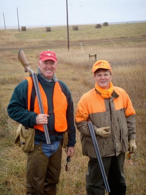 Two hunters posing with guns in a field.