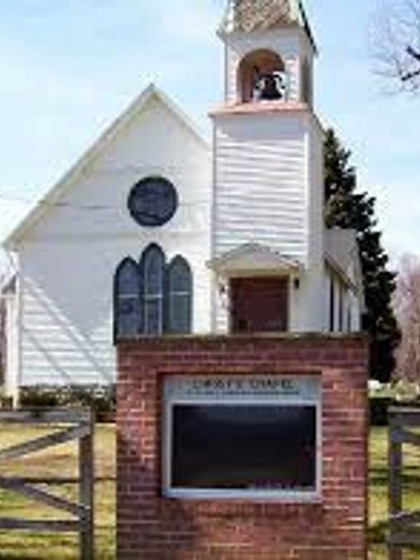 Small white church with bell tower and brick sign in front.