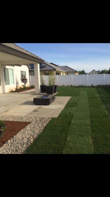 Patio con césped verde, macetas negras y plantas.