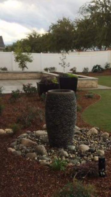 Jardín con fuente de piedra y plantas.