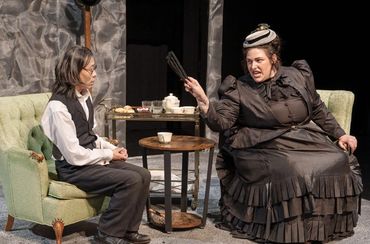 Two actors in Victorian attire engaged in a dramatic scene on stage.