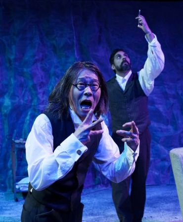 Two actors in intense, dramatic poses during a theatrical performance with blue lighting.