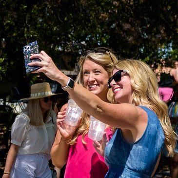 two women in pink and blue taking a selfie with the souvenir cups at magic city mimosa festival