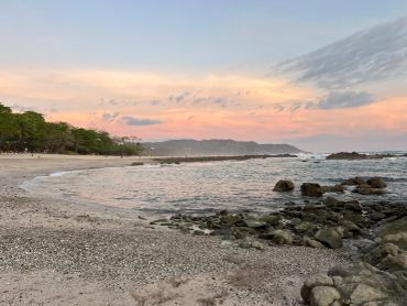 Solnedgång vid en klippig strand med rosa himmel.