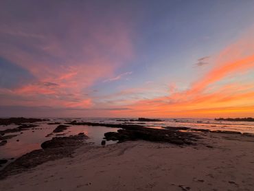 Färgglad solnedgång över strand och vatten.