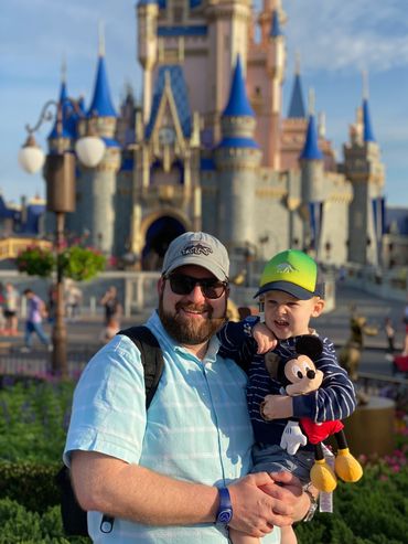 Andrew Novak holding a toddler in Disney World in front of Cinderella's castle.