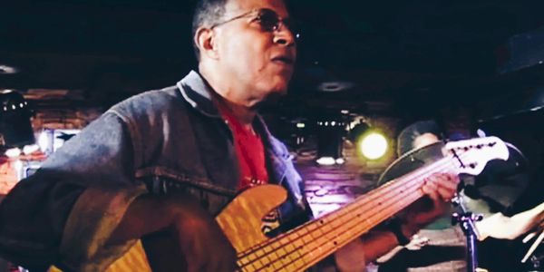 Musician playing bass guitar live on stage.