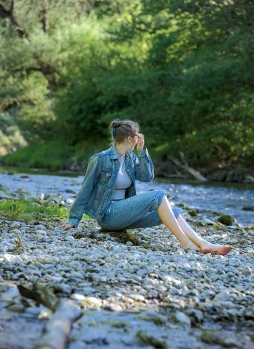 Frau am Flussufer sitzt auf Stein