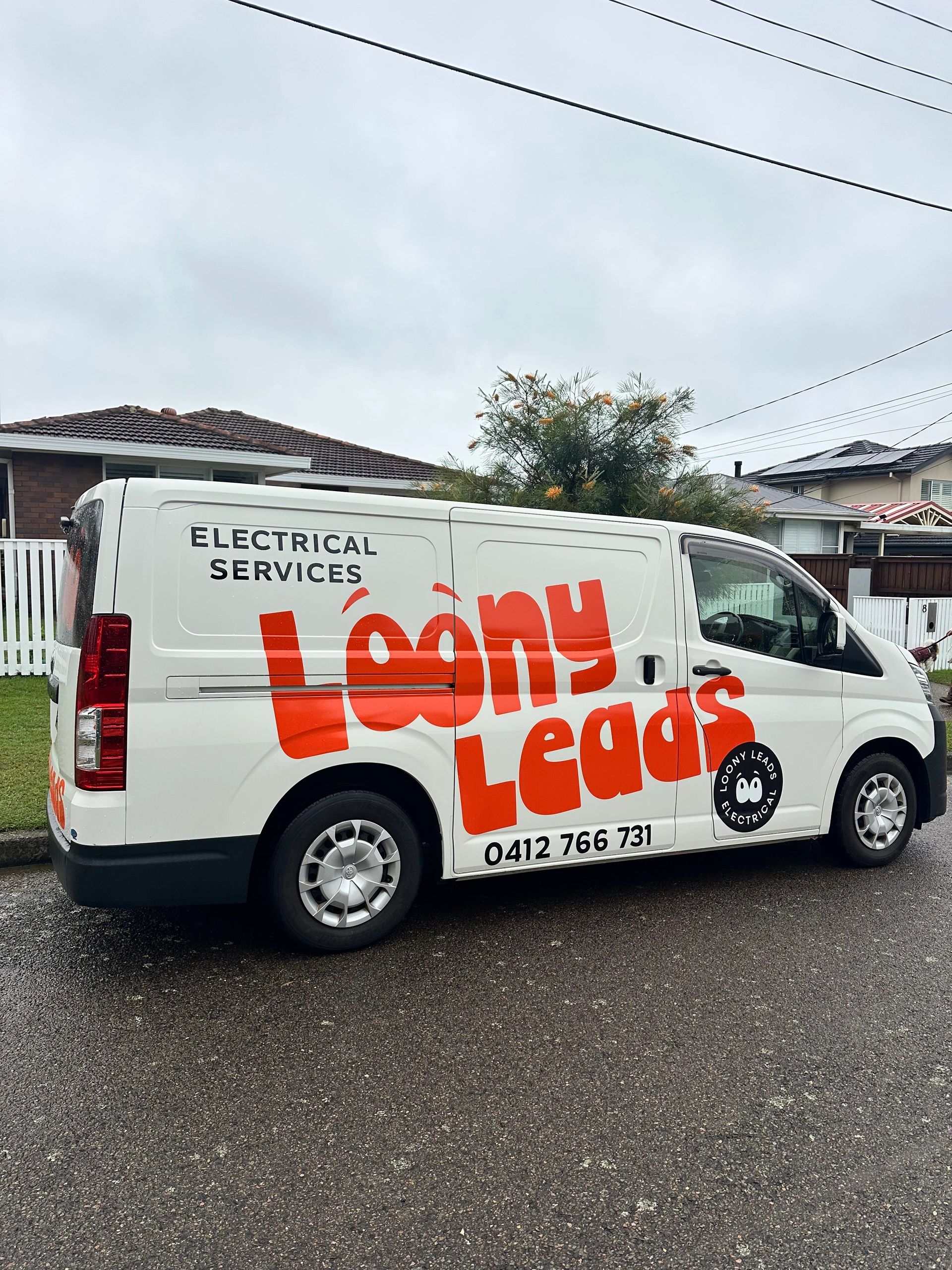White van with bright orange 'Loony Leads' electrical service branding parked on a residential street.