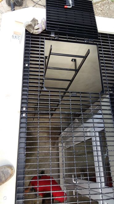 Black metal grating covers a stairwell opening with a worker below.