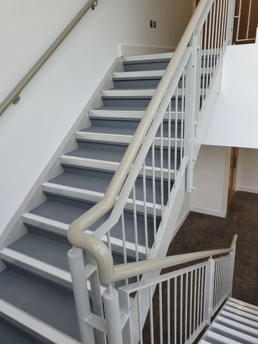 Modern indoor staircase with gray steps and beige handrails.