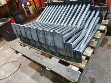 Stack of metal rods with flat plates on wooden pallet in workshop.