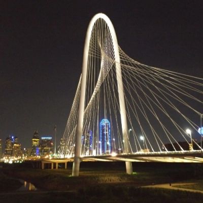 Illuminated modern bridge at night with city skyline.