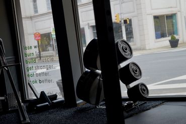 Imagen del interior de gimnasio; las ventanas y una estante con platos de pesas.