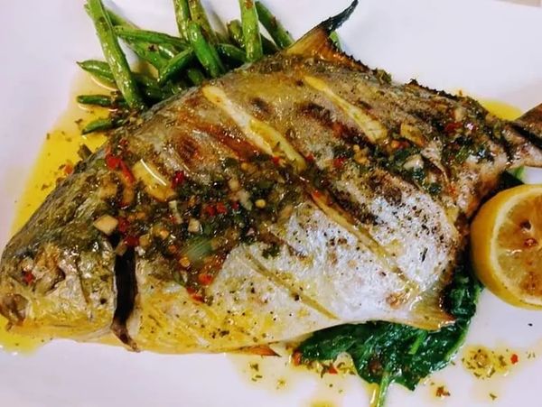Grilled whole fish served with green beans, spinach, and a lemon wedge on a white plate.