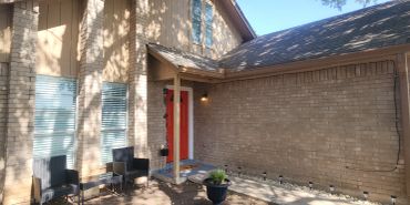Sunny brick house entrance with a red door.