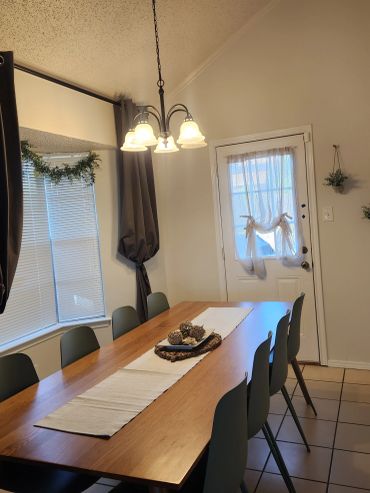 Dining room with wooden table and six chairs under hanging lights.