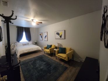 Cozy bedroom with yellow chairs, a blue rug, and framed artwork on the walls.