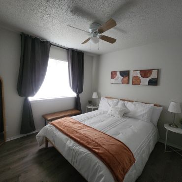 Cozy bedroom with white linens, orange throw, and modern wall art.