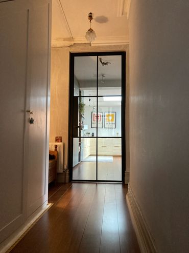 Hallway with wooden floor leading to a glass door opening into a bright kitchen.