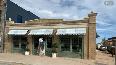 Person on ladder cleaning or repairing a window of a brick storefront.