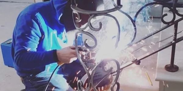 A welder in a blue hoodie working on a decorative metal staircase railing.