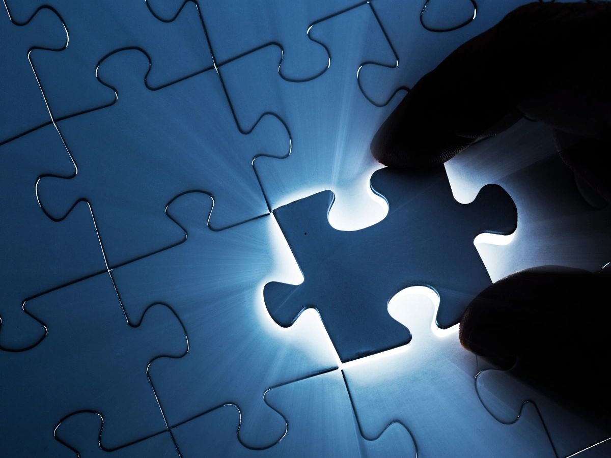 Fingers placing a glowing puzzle piece.