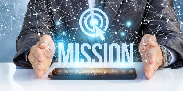 Businessman framing the word 'MISSION' with a digital target symbol above a tablet.