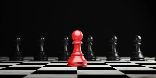 A red pawn stands out among black pawns on a chessboard.