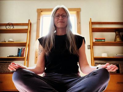 Sarah, yoga guide, seated with receiving hands open to above