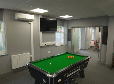 Indoor room with a pool table, TV, and glass door leading to another room.