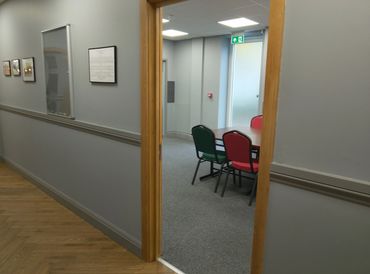 View through a doorway into a meeting room with colorful chairs around a table.