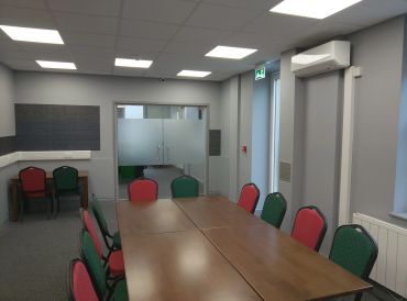 Modern conference room with wooden table and red-green chairs.