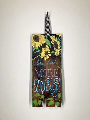 sunflowers and less bark MORE Wag painted on existential plank hanging from black and white ribbon
