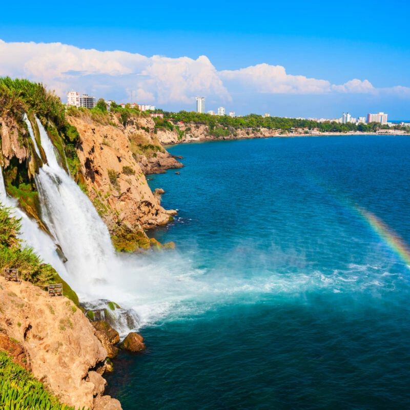 Waterfall cascading into blue sea with a rainbow over the water.